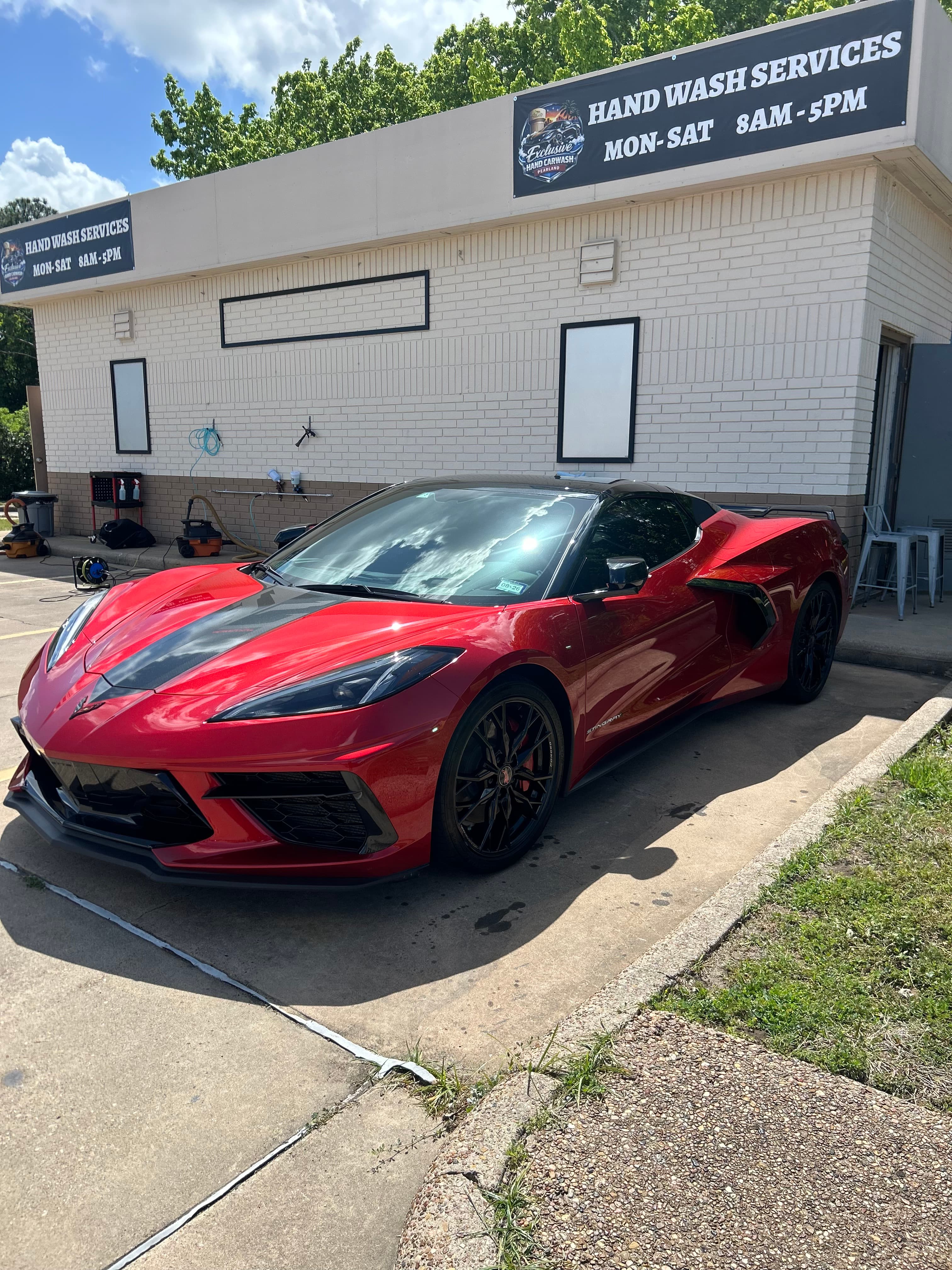 Red Chevrolet Corvette with black accents parked in front of a hand wash service building.