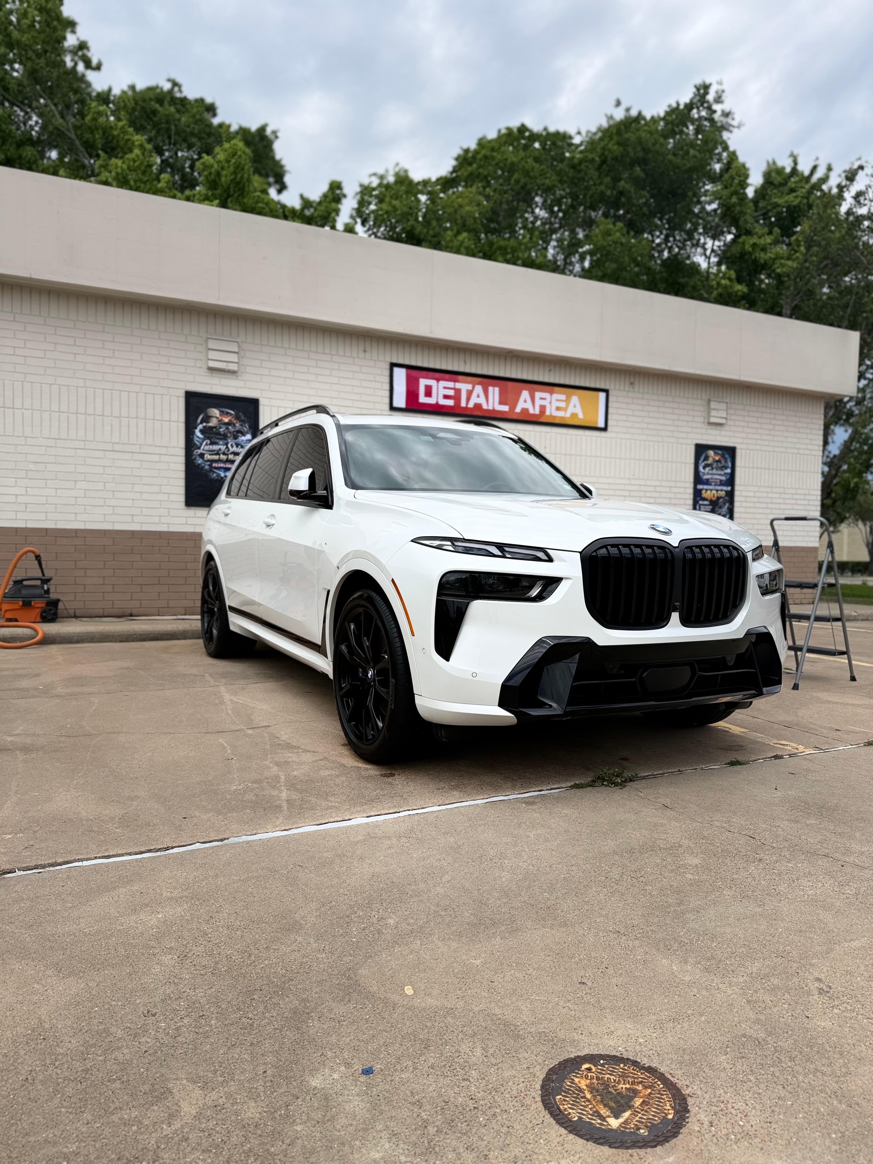 White BMW X7 SUV with black wheels parked in front of a car detailing shop.